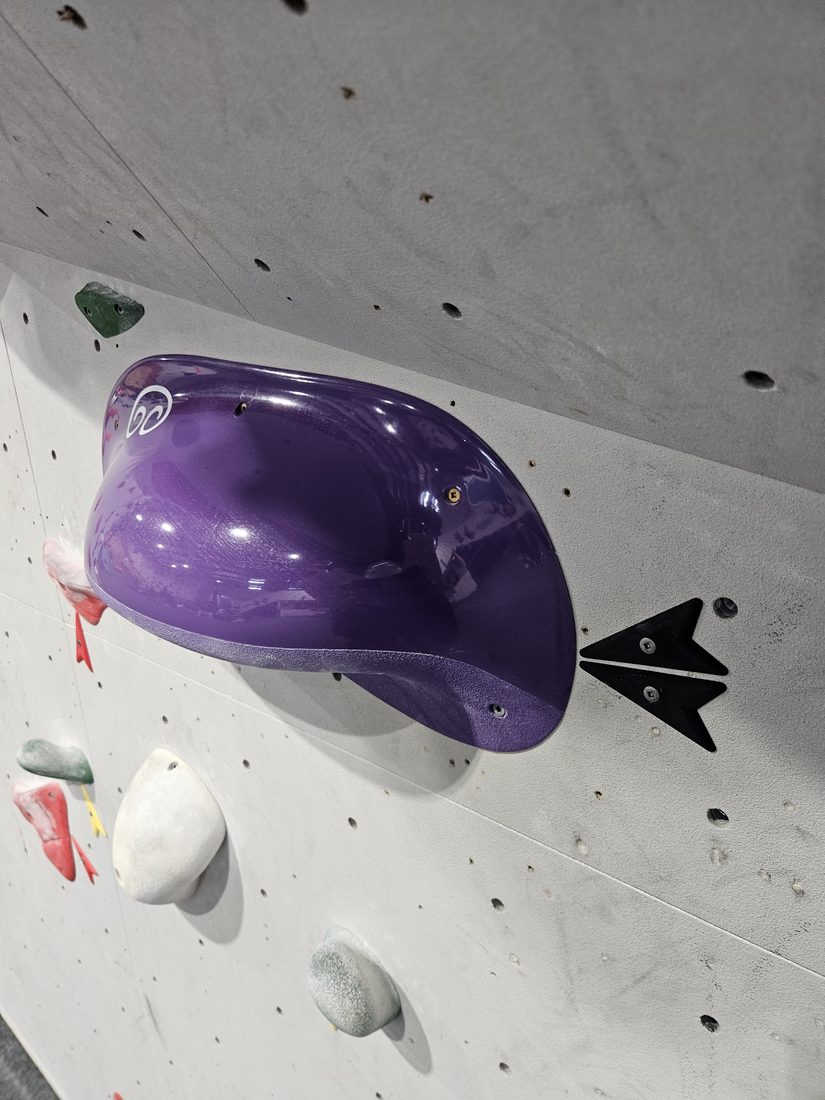 Black printed route marker above a purple climbing hold at Beta Climbing Gym.