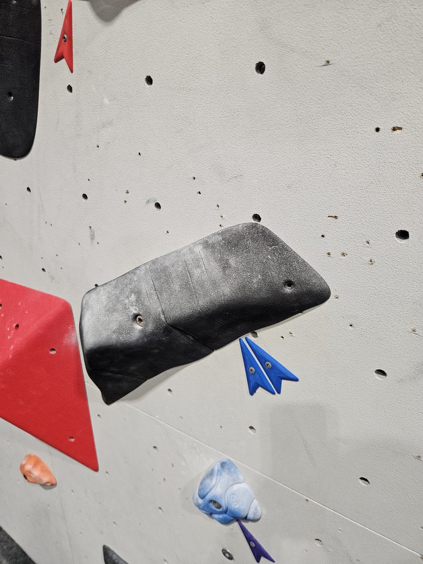 Blue printed route marker beside a black climbing hold at Beta Climbing Gym.