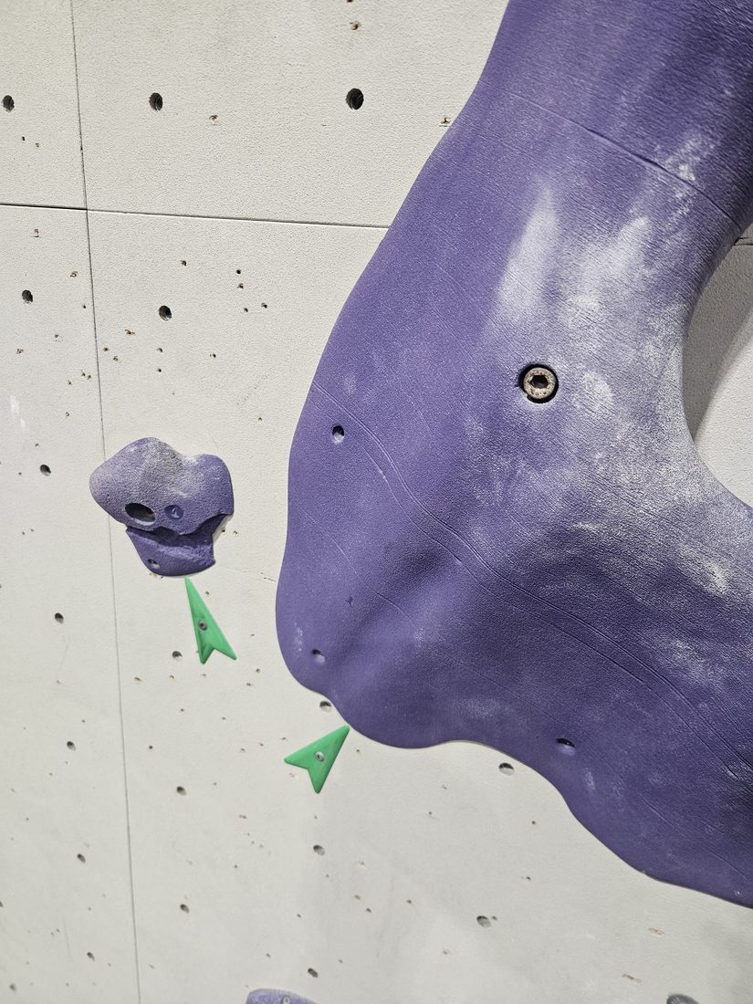 Green printed route marker beside a purple climbing hold at Beta Climbing Gym.