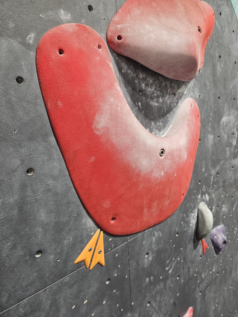Orange printed route marker beside a red climbing hold at Beta Climbing Gym.