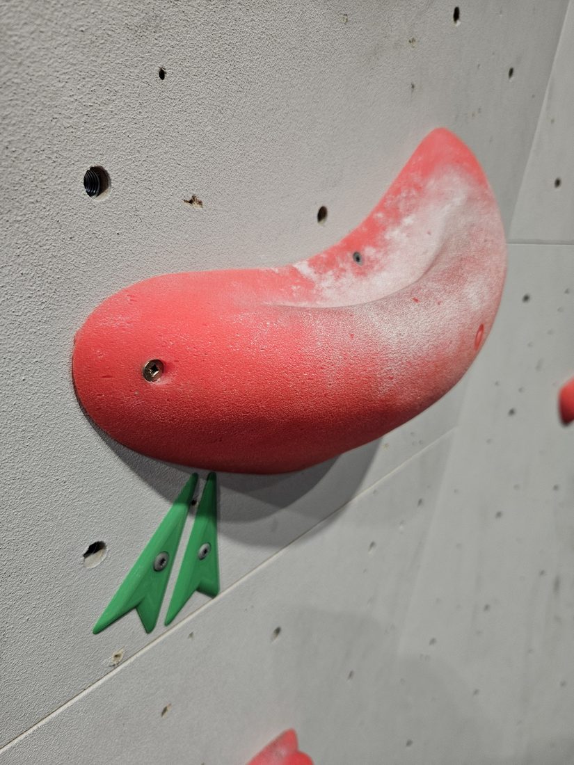 Green printed route marker behind a red climbing hold at Beta Climbing Gym.