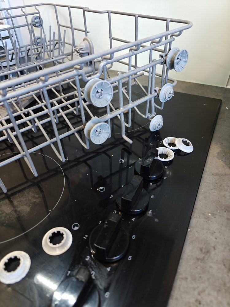 3D printed dishwasher basket wheel replacements installed on a rack.