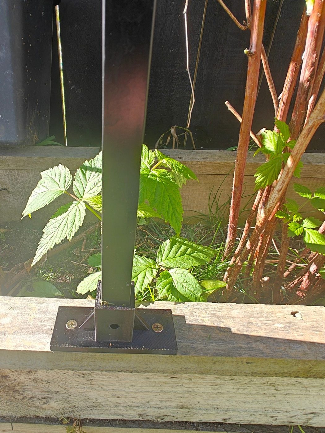 Close-up of a printed base mount screwed to a garden bed with a black aluminium post.