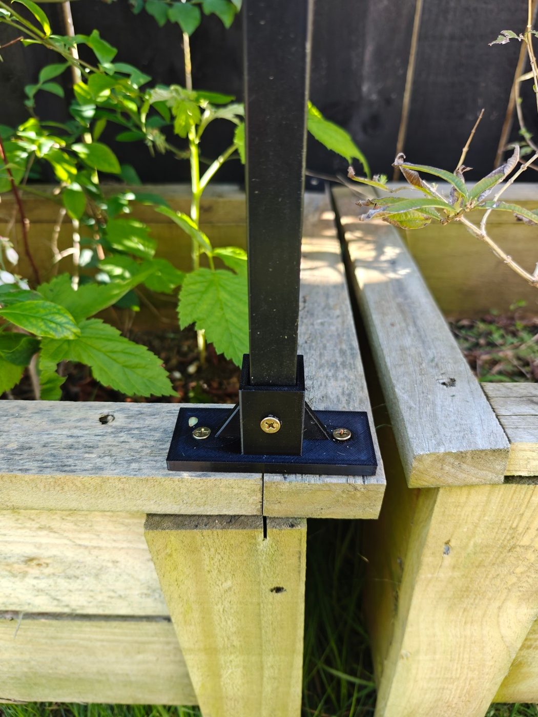 Printed base mount screwed to the corner of a timber garden bed, holding a black aluminium post.