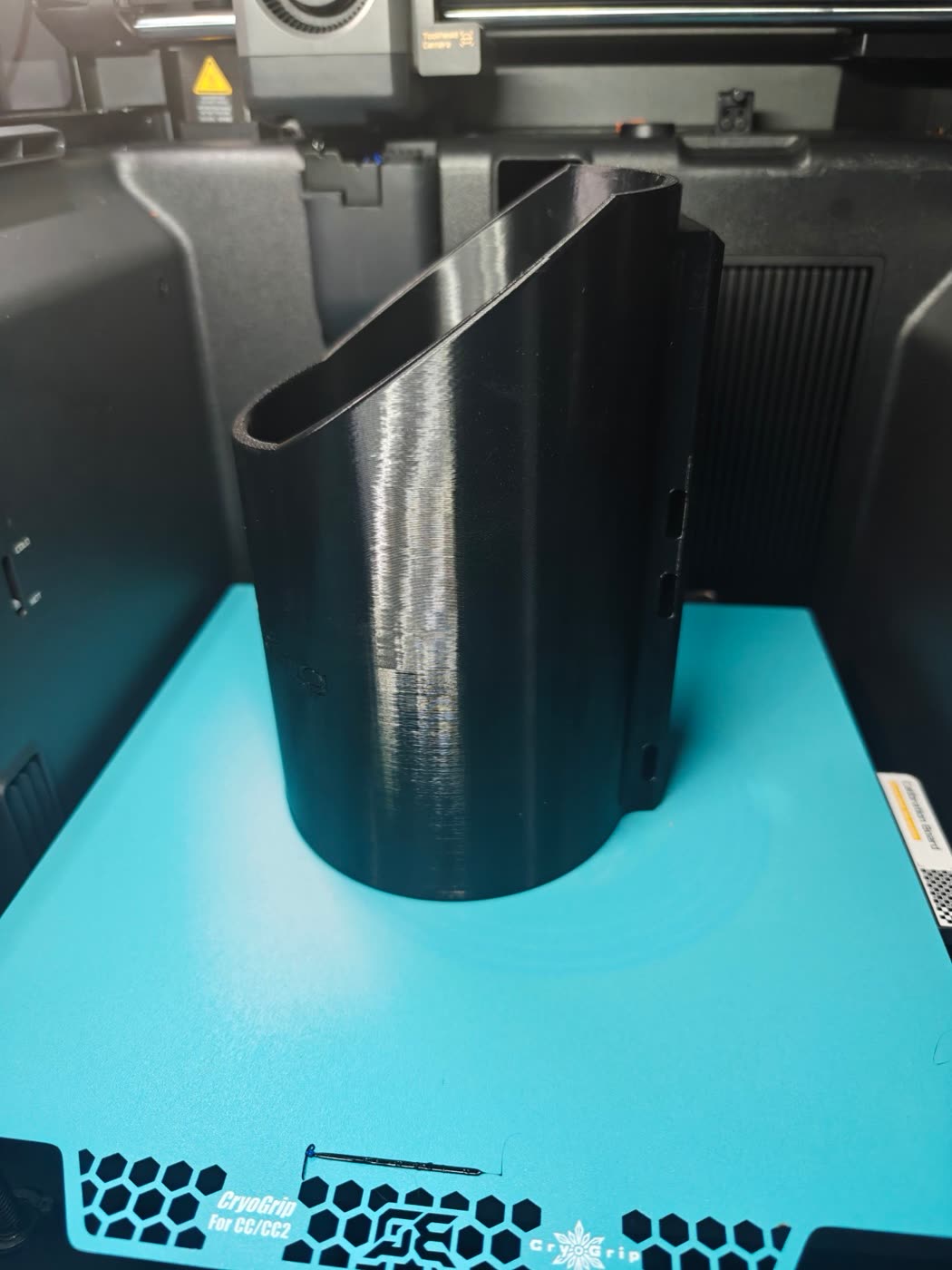 Side view of the black printed bottle holder showing the angled top and the rear mounting plate with three slots.