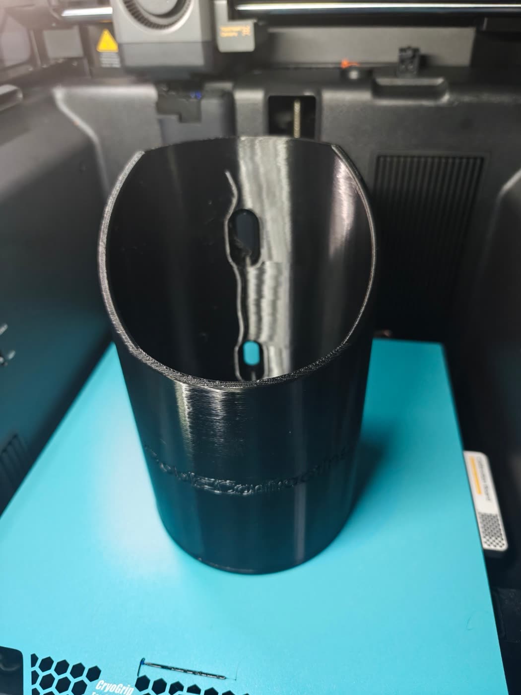 Looking into the black printed bottle holder, showing the slotted mounting holes and the engraved company name on the side.