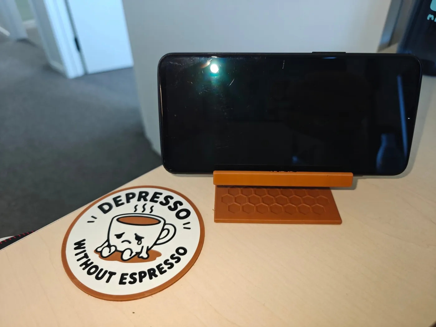Phone resting on its side in the Q3D phone stand, next to a Depresso Without Espresso coffee coaster.