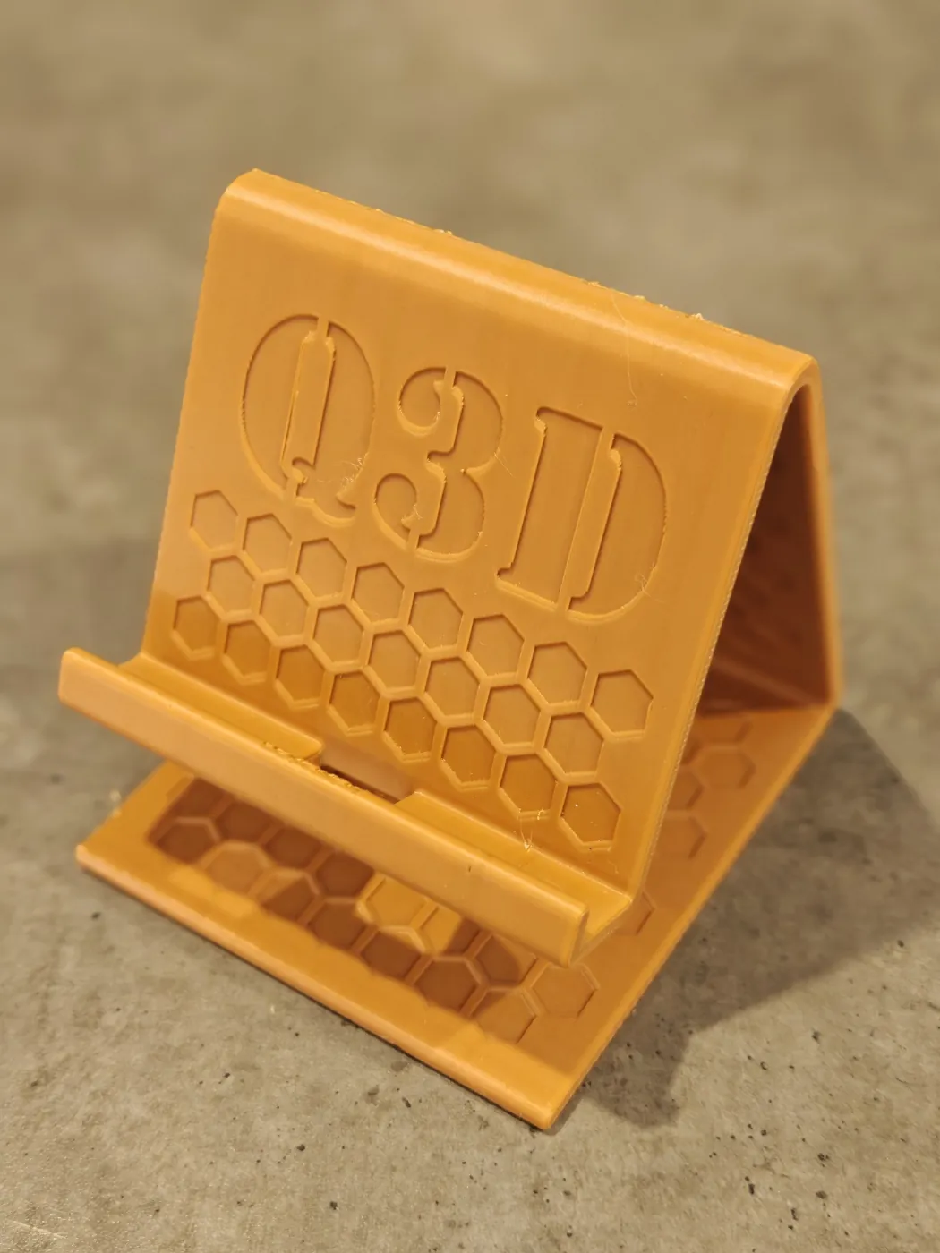 Close-up of the Q3D logo and hexagon pattern on the front face of the empty phone stand.